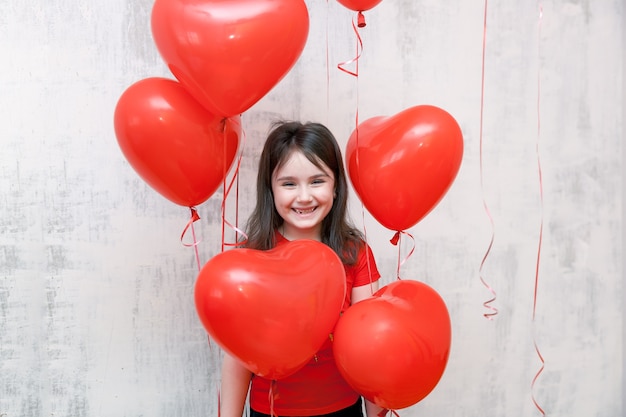 lachende meisje permanent onder rode helium hartvormige ballonnen op een witte achtergrond