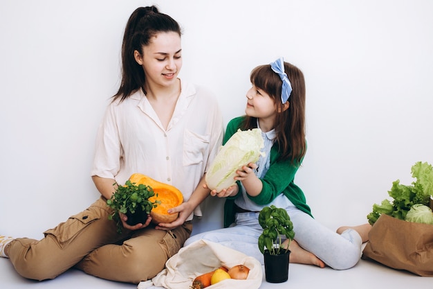 Lachende meisjes met een papieren eco-zak met gezonde groenten en groenten, geïsoleerd op wit. Gezond eetconcept. Geen afvalconcept. Pakketvrij boodschappen doen. Eco vriendelijke natuurlijke tas met biologische fr