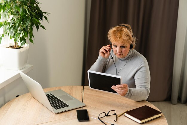 Lachende moderne volwassen 60s blanke vrouw in oortelefoons kijken webinar online thuis. Gelukkige senior grijsharige vrouw veel plezier met studeren op internet. Ouderen technologie concept.