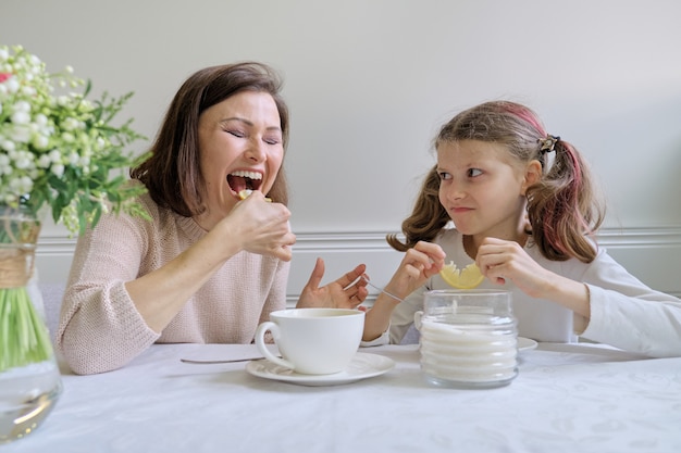 Lachende moeder en dochter die van koppen drinken en citroen eten.