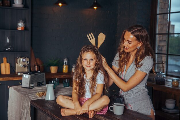 Lachende moeder en dochter koken en plezier maken in het donkere keuken interieur