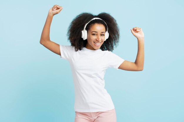 Foto lachende mooie afro-amerikaanse vrouw met krullend haar luisteren naar muziek in koptelefoon dansen