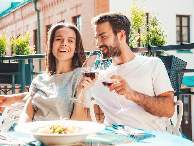 Lachende mooie vrouw en haar knappe vriendje Gelukkige vrolijke familie Paar juichen met glazen rode wijn op hun date in restaurant Ze drinken alcohol in veranda café in de straat