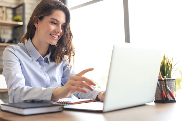 Lachende mooie vrouw zittend aan tafel, kijkend naar het scherm van de laptop. Gelukkige ondernemer die bericht-e-mail leest met goed nieuws, online chat met klanten.