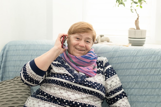 Lachende oudere vrouw thuis met een mobiele telefoon in haar handen Positieve emoties Thuisleven