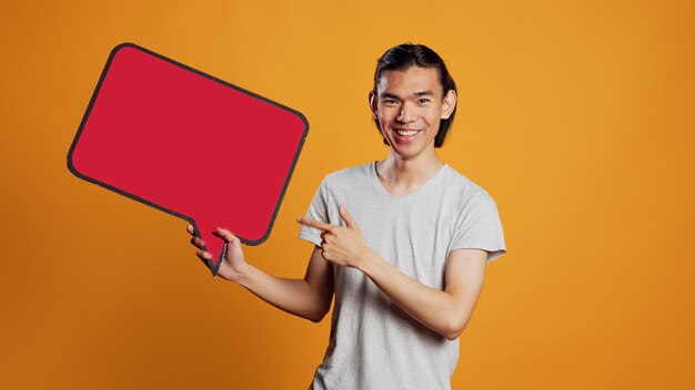 Lachende persoon met rode tekstballon met copyspace, met behulp van kartonnen pictogram met geïsoleerde ruimte voor bericht. Vrolijke jongeman kartonnen billboard op camera, leeg bord tonen.