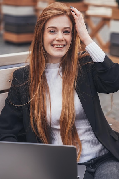 Lachende roodharige mooie zakenvrouw werken met laptop op houten bankje in het park Positieve persoon Kinderen levensstijl kindertijd concept