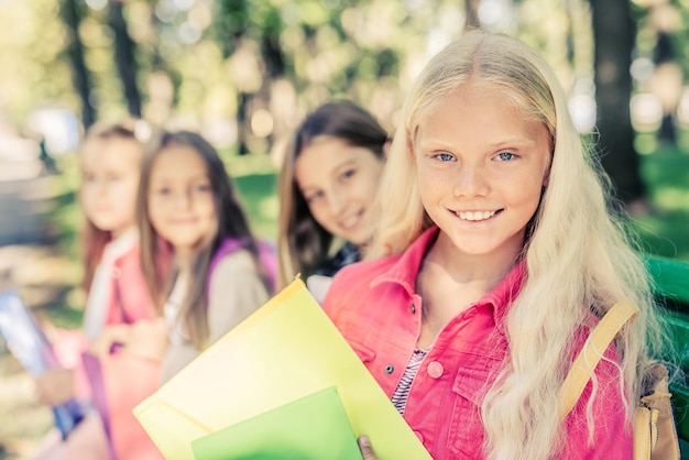 Foto lachende schoolmeisjes met schoolspullen zitten op de bank