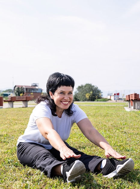 Lachende senior vrouw warming-up die zich uitstrekt buiten in het park