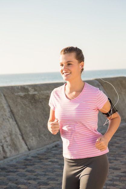 Lachende sportieve blonde joggen met een koptelefoon