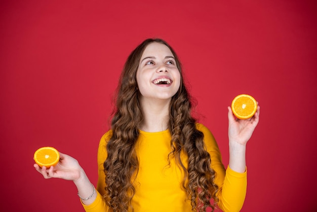 Lachende tienermeisje houdt oranje fruit op paarse achtergrond