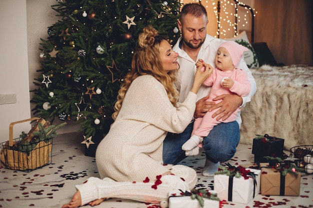 Lachende vader en moeder kijken naar hun schattige baby in de buurt van de kerstboom