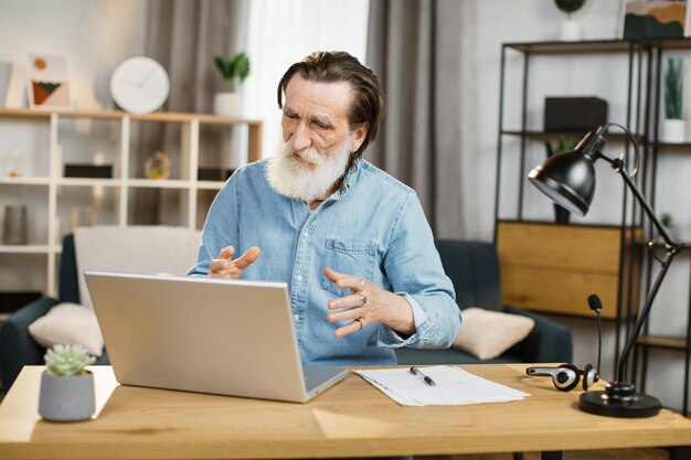 Lachende volwassen zakenman met behulp van moderne laptop voor video-chat op afstand werken