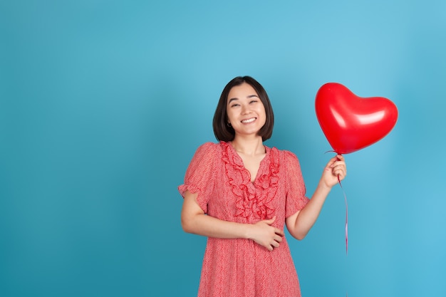 lachende, vrolijke jonge Aziatische vrouw houdt een vliegende rode hartvormige ballon