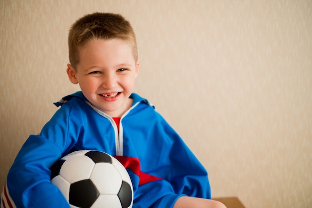 Lachende vrolijke jongen met een voetbal in een blauwe sport uniform.