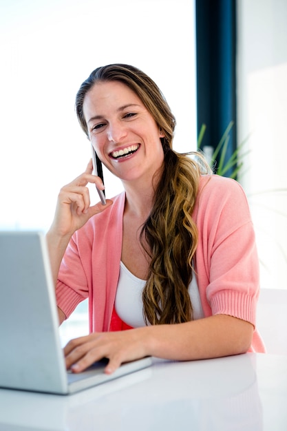 lachende vrouw aan haar bureau op haar laptop en mobiele telefoon