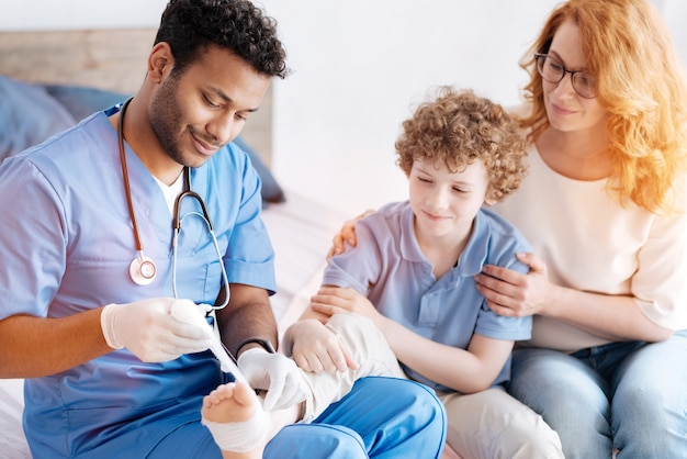 Lachende vrouw achter haar zoon zitten terwijl ze hem omhelzen en kijken naar gewonde been