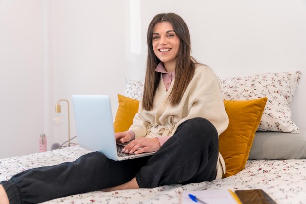Lachende vrouw die werkt met laptop zittend op bed telewerken telewerken