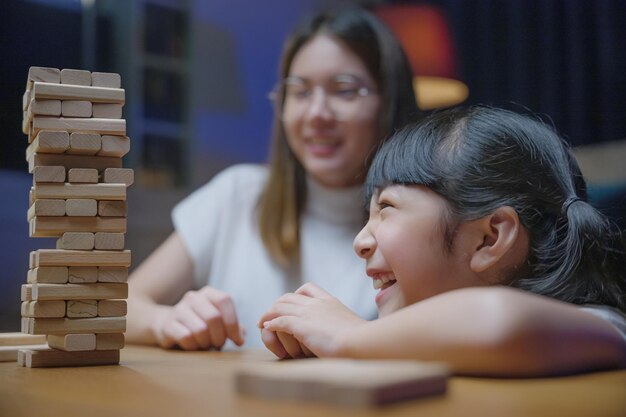 Lachende vrouw helpt kind te leren bouwen constructeur van houten blokken, Aziatische jonge moeder speelt spel in houtblok met haar dochtertje in huis woonkamer 's nachts voordat ze naar bed gaat