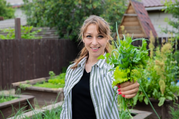 lachende vrouw houdt boeket van groene uien, peterselie en slablaadjes in de tuin