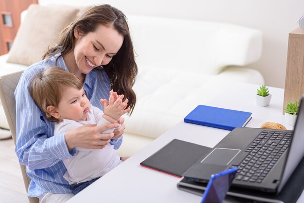 Lachende vrouw in blauw shirt met kind zittend op laptop palm spelen