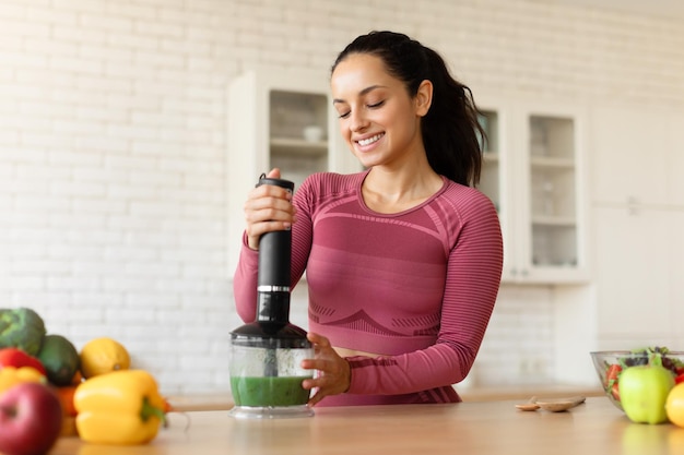 Lachende vrouw in fitwear smoothie maken met blender in de keuken