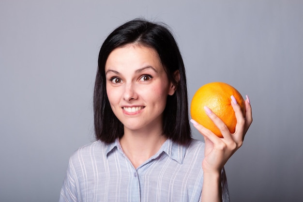 lachende vrouw in oranje shirt met grapefruit in haar handen
