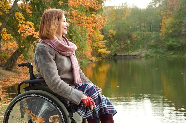 Lachende vrouw in rolstoel genieten van prachtig uitzicht op het meer in het park op herfstdag