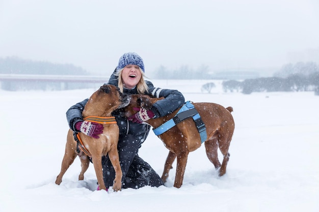 Lachende vrouw knuffelen met boxerhonden tijdens een wandeling in de sneeuw Favoriete huisdieren liefde en vriendschap