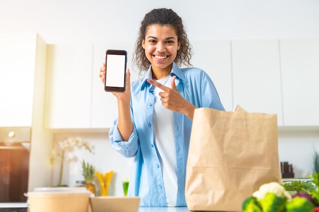 Lachende vrouw met boodschappentas online besteld via smartphone en direct thuisbezorgd