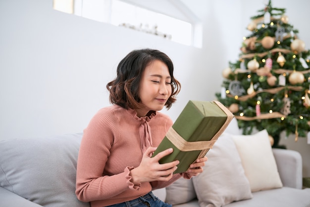 Lachende vrouw met geschenkdoos tegen de achtergrond van de kerstboom. Gelukkige jonge vrouw die Kerstmis viert