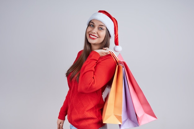 Lachende vrouw met kerstmuts, rode trui, boodschappentassen te houden. Het concept van kerstverkopen, winkelen, kortingen.