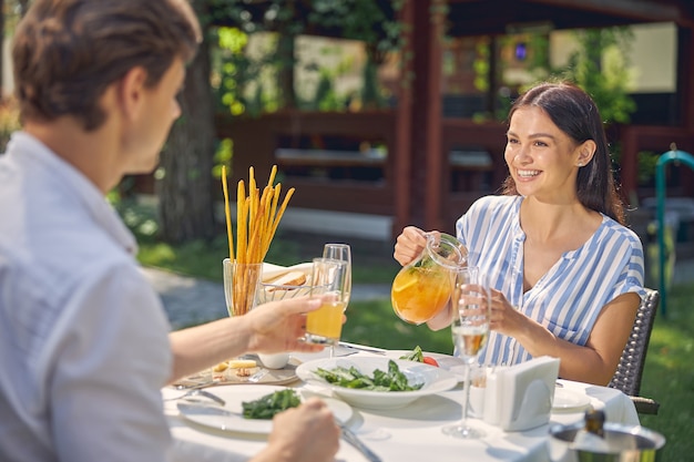 lachende vrouw met sinaasappellimonade in de hand terwijl ze naar de man aan tafel in restaurant kijkt