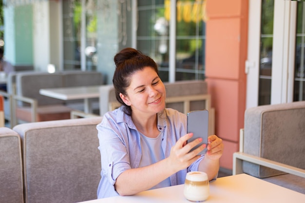 Lachende vrouw met smartphone en koffiekopje buiten