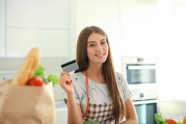 Lachende vrouw online winkelen met behulp van computer en creditcard in de keuken.