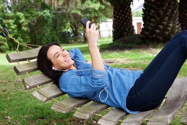 Lachende vrouw ontspannen op hangmat met mobiele telefoon