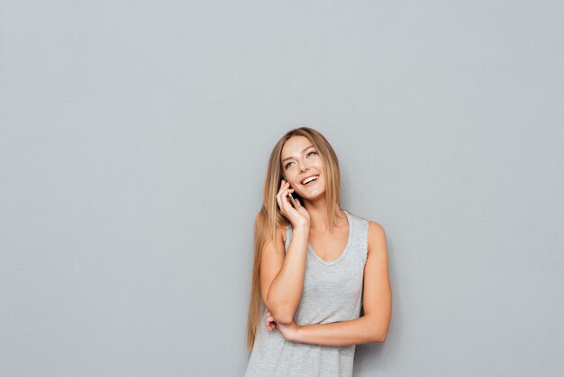 Lachende vrouw praten over de slimme telefoon geïsoleerd op een grijze achtergrond