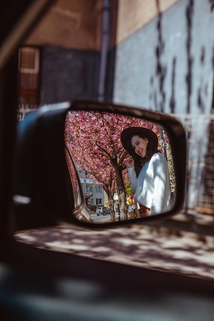 Lachende vrouw reflectie in auto achteruitkijkspiegel bloeiende sakura boom op achtergrond lente komt eraan