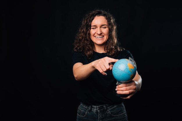 Lachende vrouw wijst naar haar volgende bestemming op een kleine Earth Globe