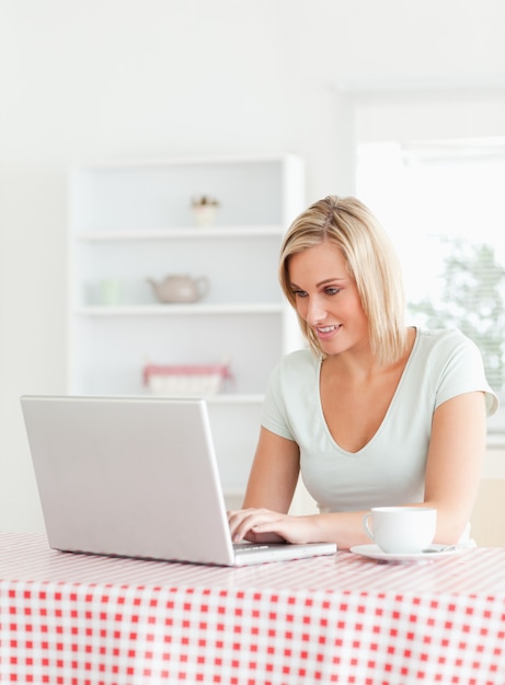 Lachende vrouw zitten aan een tafel met een kopje koffie en een notebook