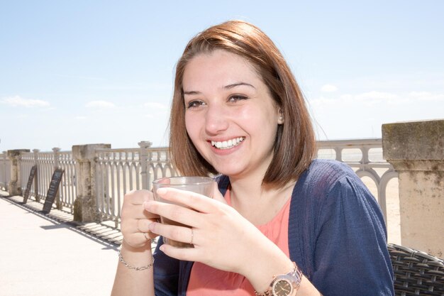 Lachende vrouw zittend op het strand met een kopje warme drank