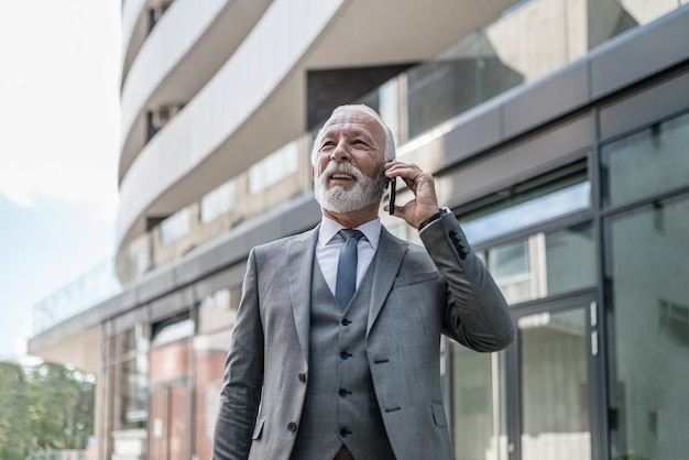 Lachende zakenman die op een smartphone praat terwijl hij buiten het kantoorgebouw staat