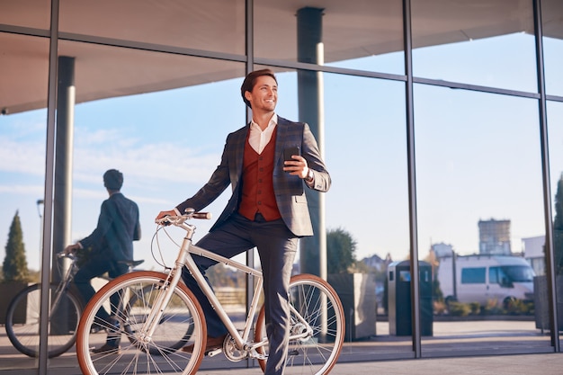 Lachende zakenman met telefoon en fiets op stadsstraat