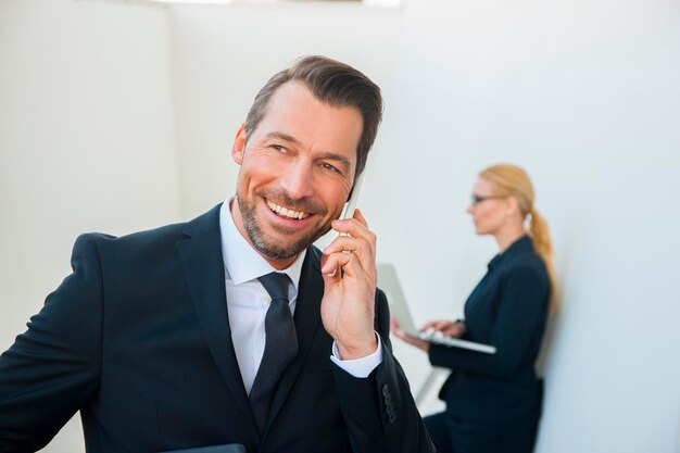 Foto lachende zakenman op mobiele telefoon en zakenvrouw met behulp van laptop buitenshuis