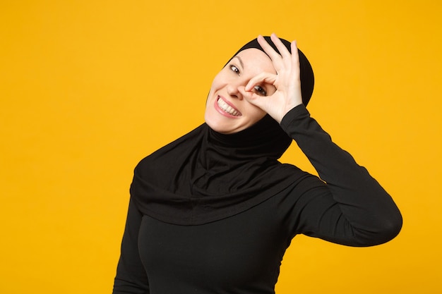 Lachende zelfverzekerde mooie jonge Arabische moslimvrouw in hijab zwarte kleding poseren geïsoleerd op gele muur, portret. Mensen religieuze islam levensstijl concept.