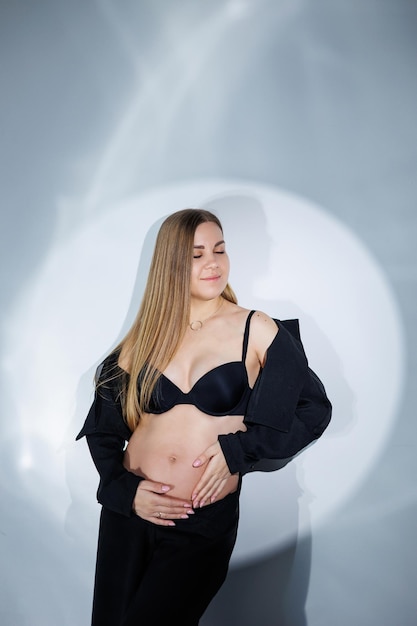 Lachende zwangere vrouw in een zwart pak op een grijze achtergrond Mooie elegante zwangere vrouw