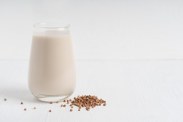 Lactosevrije gezonde boekweitmelk geserveerd in hoog drinkglas met granen op witte houten tafel