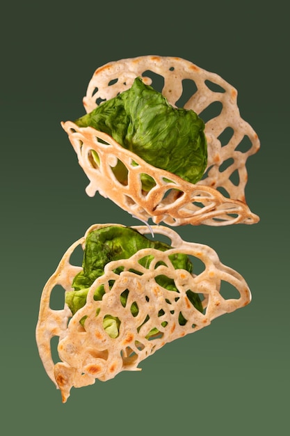 Lacy pancakes with lettuce leaves fly on a green background