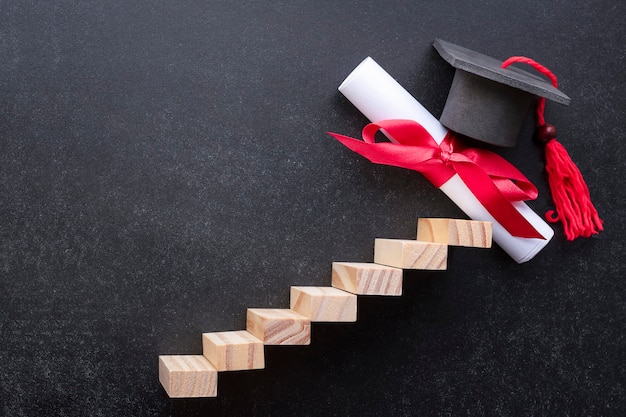 Photo ladder and diploma with graduate cap on black background