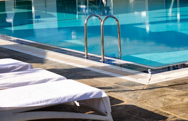 Ladder stainless handrails for descent into swimming pool and
nice beach chairs sun beds with a white towels metal handrails and
blue water at sunrise steps into the open air swimming pool
summer